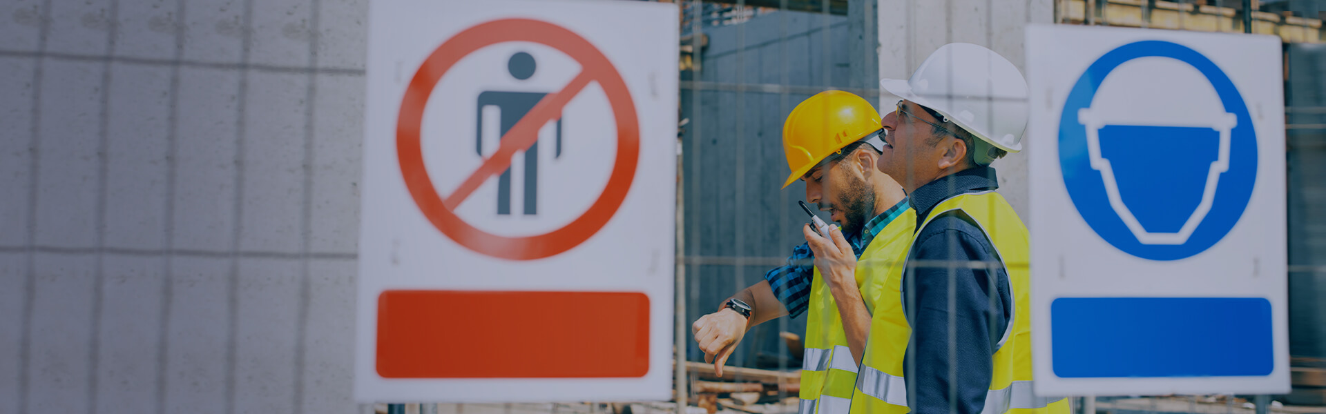Image of two construction workers with construction site warning signs to wear a hard hat, and no unauthorised persons in the foreground