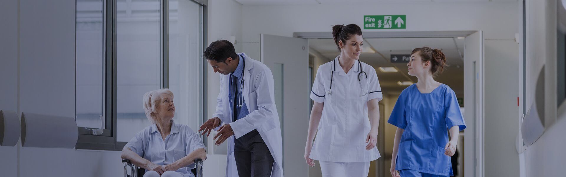 Image of two health staff walking down a corridor, and another speaking to a patient in a wheelchair